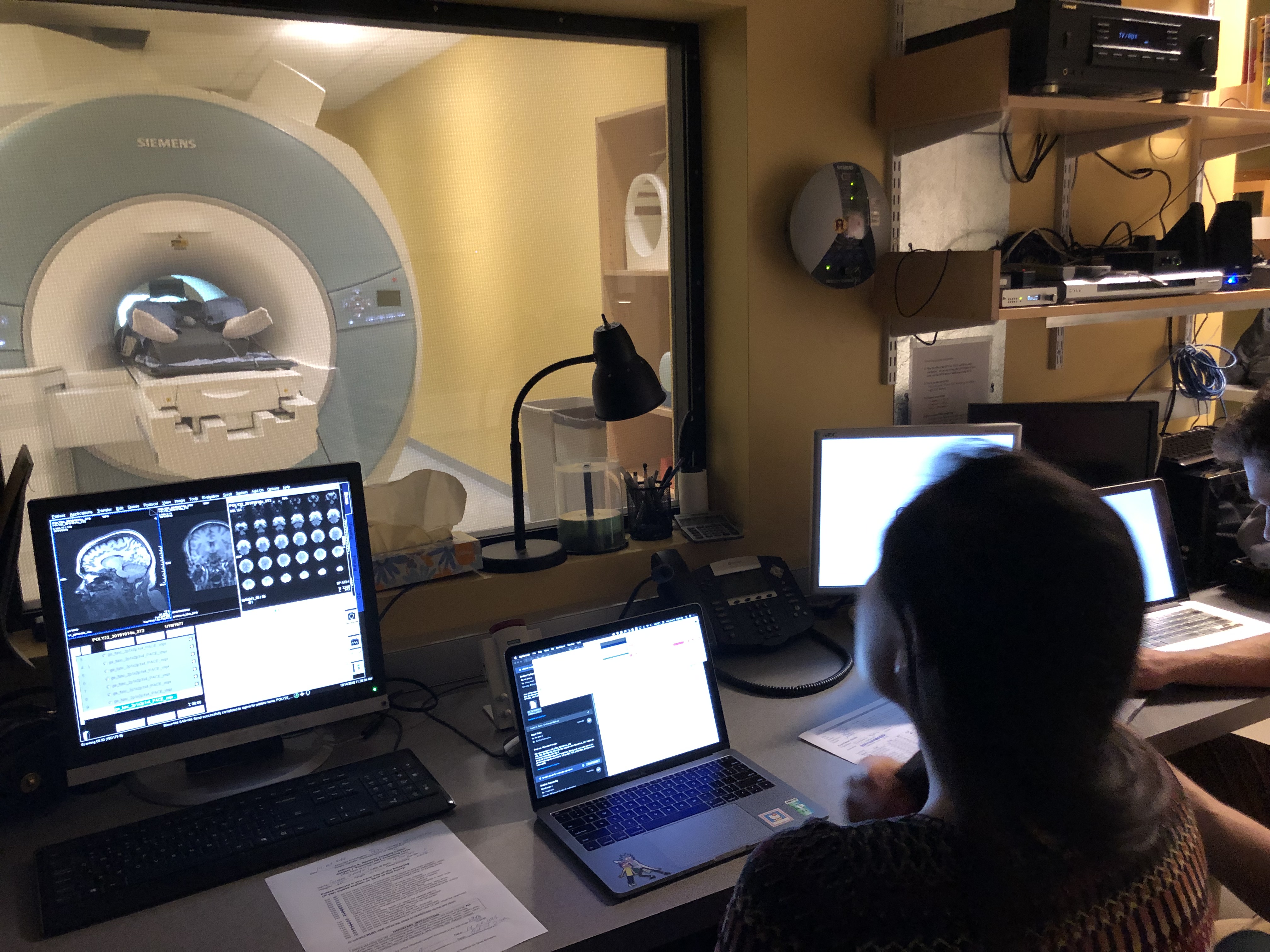 Photo of feet sticking out of fMRI machine and the lab technician in the control room with computer screens