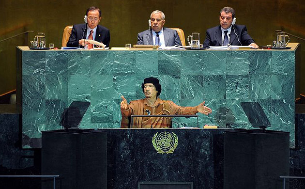 Muammar Gaddafi with his hands up. 3 UN people behind him